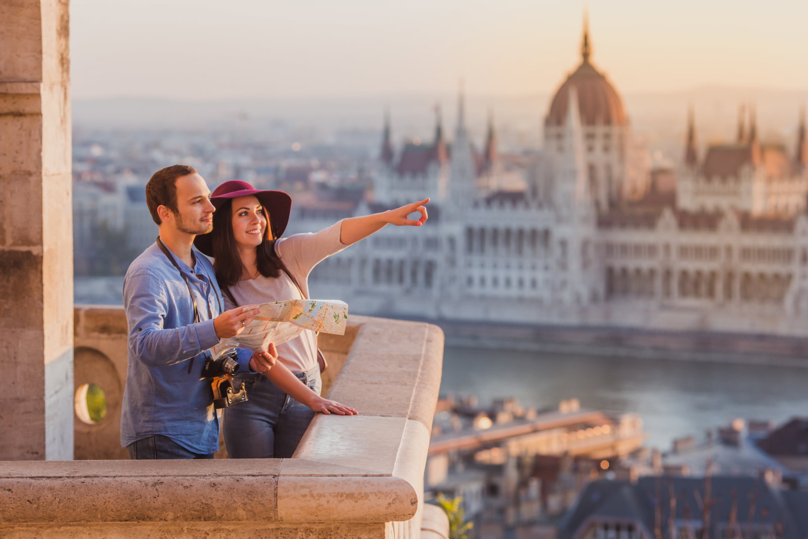 Paar mit Stadtplan blickt bei Sonnenuntergang über die Donau auf das Budapester Parlament